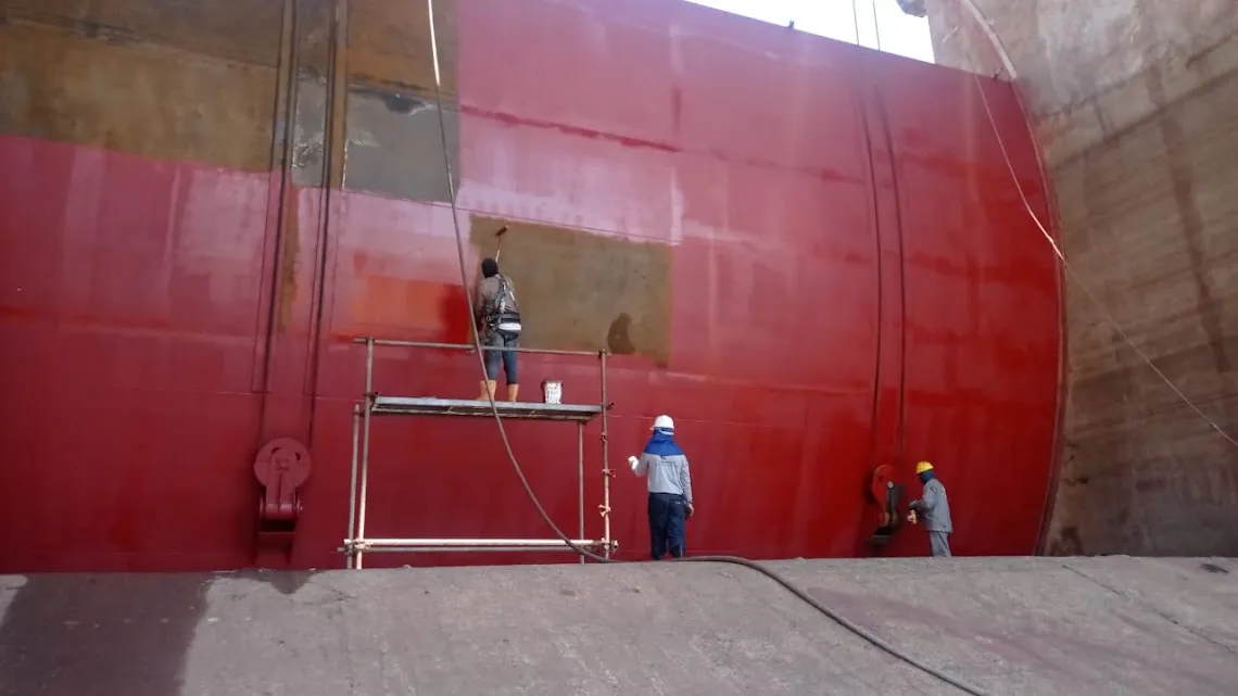 Três trabalhadores aplicando tinta vermelha com rolo e trincha sobre a face de montante de uma comporta, com andaime móvel ao centro.