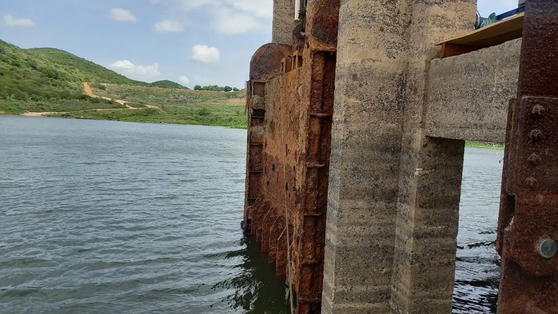 Estrutura metálica fortemente corroída junto ao pilar de concreto da tomada d'água, parcialmente submersa no reservatório.