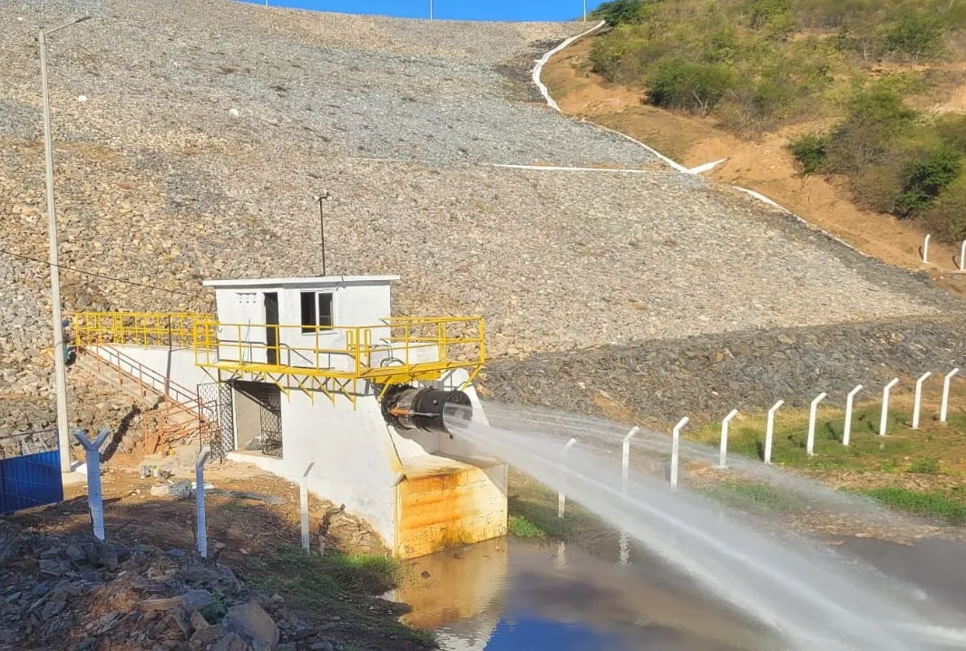 Válvula dispersora descarregando jato de água a partir da casa de comando branca, no pé do talude de enrocamento da Barragem dos Prazeres.